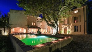 Un patio con piscina, un árbol y un edificio de fachada de piedra y ventanas de arco.