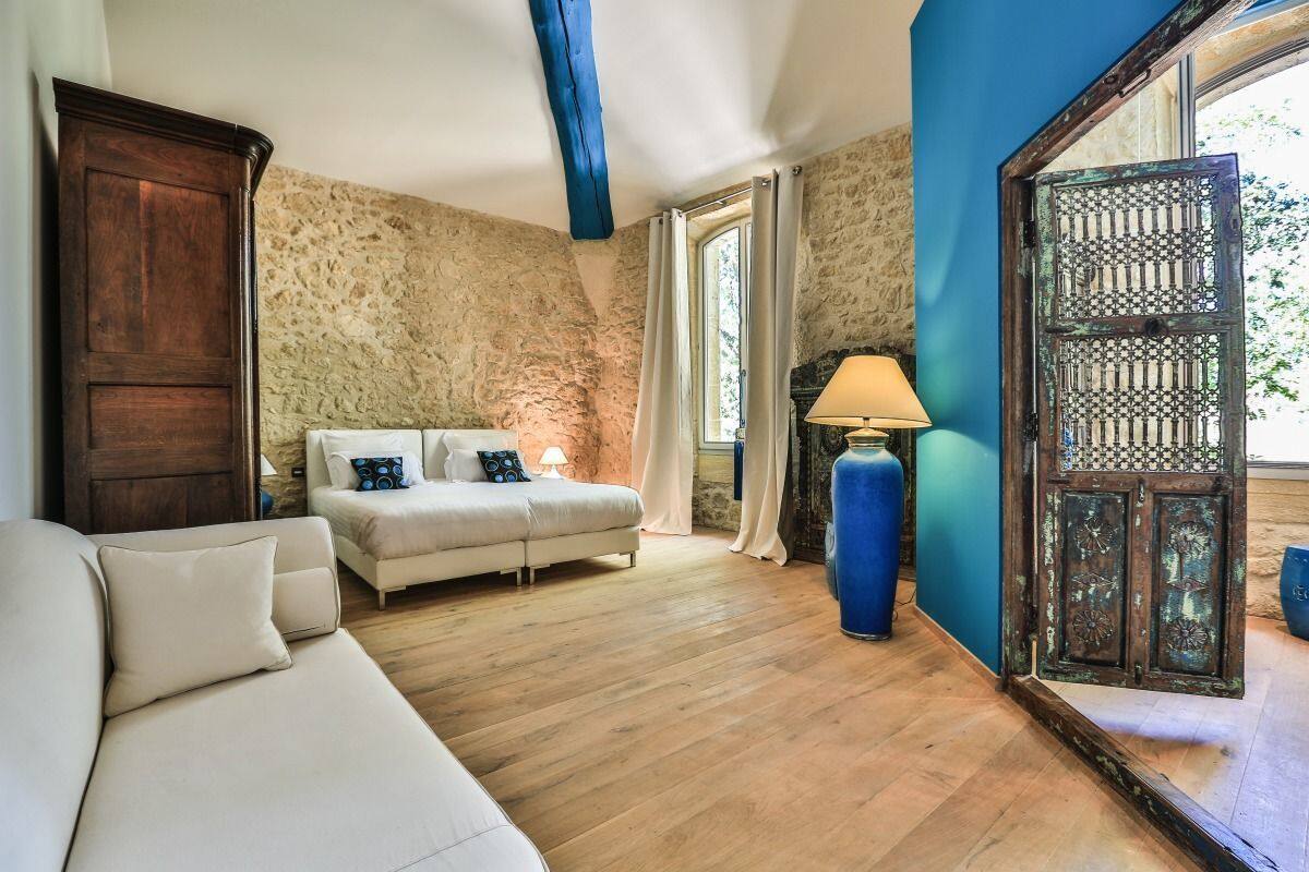 A room with a wooden floor, a white sofa, a bed with pillows, a lamp, and a large window with curtains.
