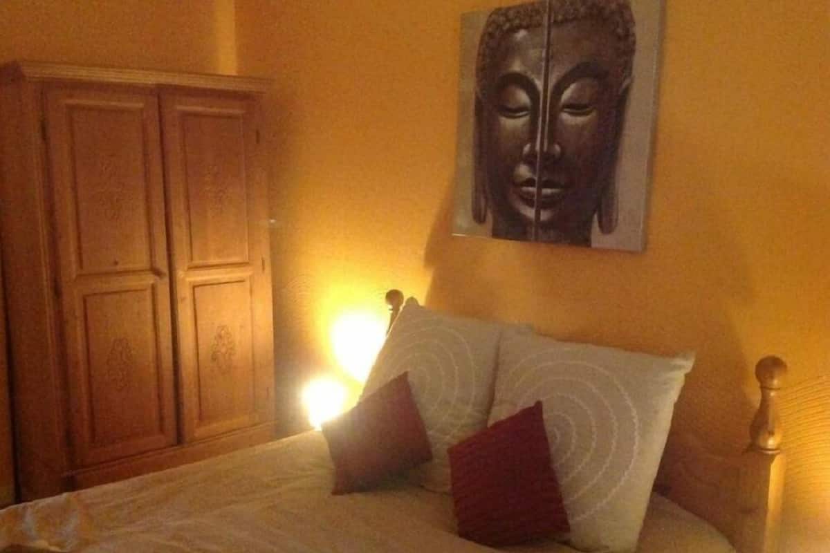 Un dormitorio con una cama, almohadas, un armario de madera y una estatua de Buda en la pared.