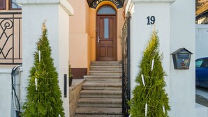 A building entrance with a wooden door, a number '19' on the wall, and two potted Christmas trees. - Casa Moritz (Brasov)