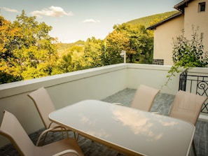 Un balcon avec une table et des chaises, donnant sur une colline boisée.