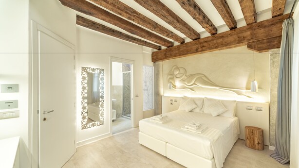A modern bedroom with a large bed, wooden beams on the ceiling, and a decorative wall piece. - Ca' de la Fonte | WENICE Deep Culture (Venice)
