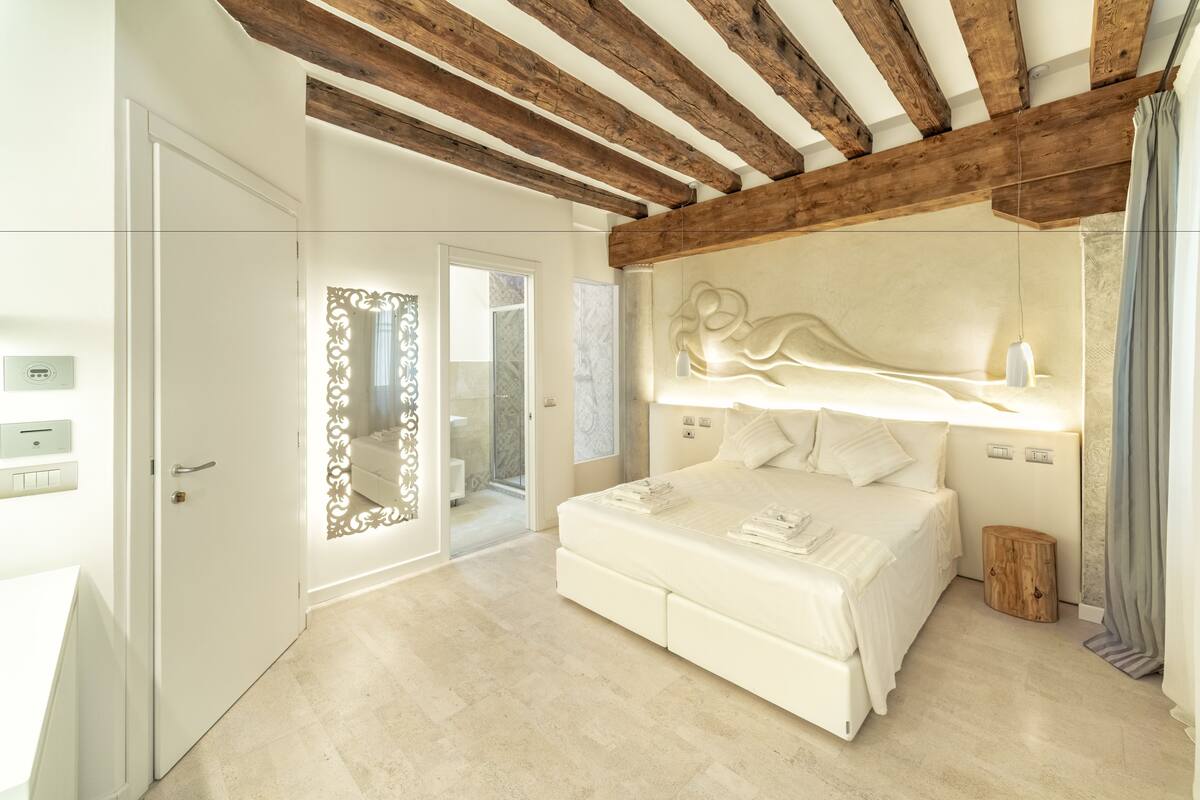 A modern bedroom with a large bed, wooden beams on the ceiling, and a decorative wall piece.