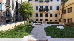 A courtyard with a central fountain, surrounded by neatly trimmed hedges and a brick pathway leading to a set of stairs. - Ca' de la Fonte | WENICE Deep Culture (Venice)