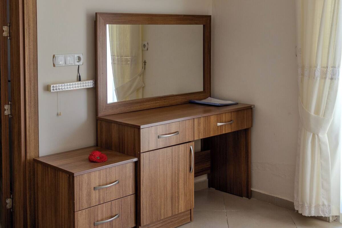 A bedroom with a wooden desk, a mirror, a bedside table, and a bed.