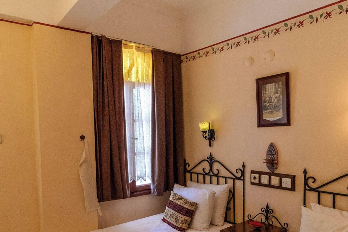 A hotel room with two beds, a window with curtains, a wall-mounted light, and a framed picture.