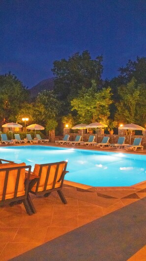 A swimming pool with lounge chairs and umbrellas, surrounded by trees and a stone wall. - Yakamoz Hotel Fethiye (Fethiye)