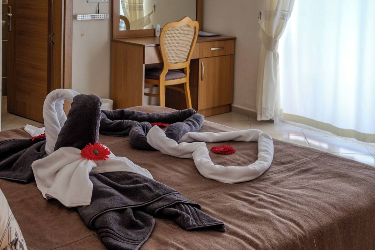 A hotel room with a bed, a desk, a chair, a mirror, and a window with curtains.