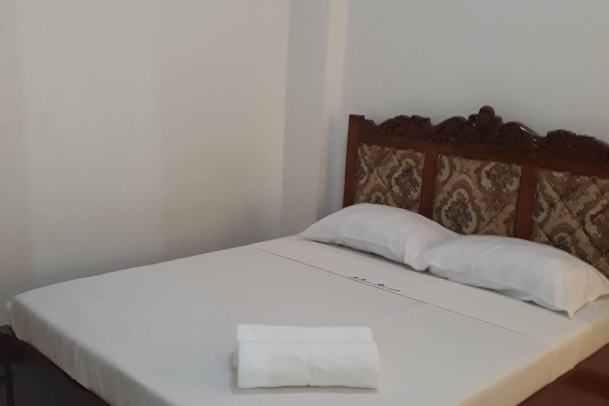 A single bed with a wooden headboard, white bedding, and a neatly folded white towel on the bed.