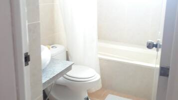Un baño pequeño y estrecho con inodoro, zona de ducha y lavamanos.