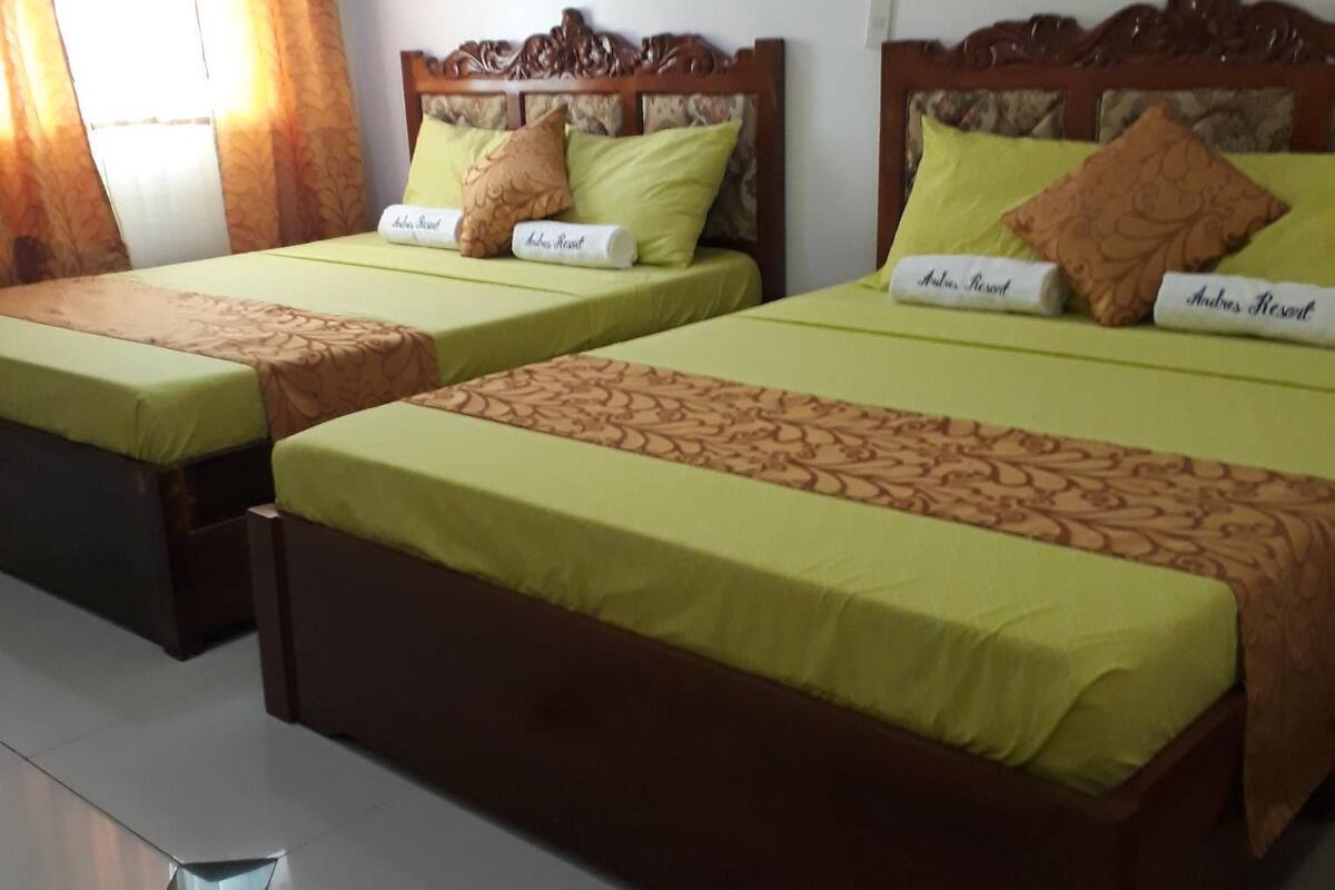 A hotel room with two single beds, each with a wooden headboard and green bedding.