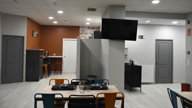 Een moderne eetruimte met een lange tafel, stoelen en een aan de muur bevestigde televisie.
