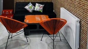 Een compacte kamer met een zwarte bank, twee oranje stoelen en een radiator.