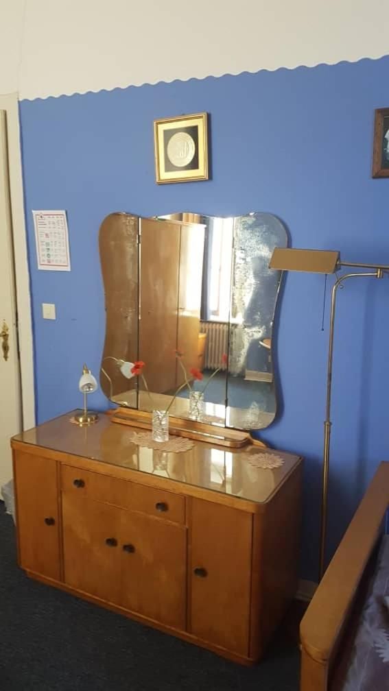 Una habitación con un aparador de madera, un espejo grande, una lámpara de pie y un cuadro en la pared.
