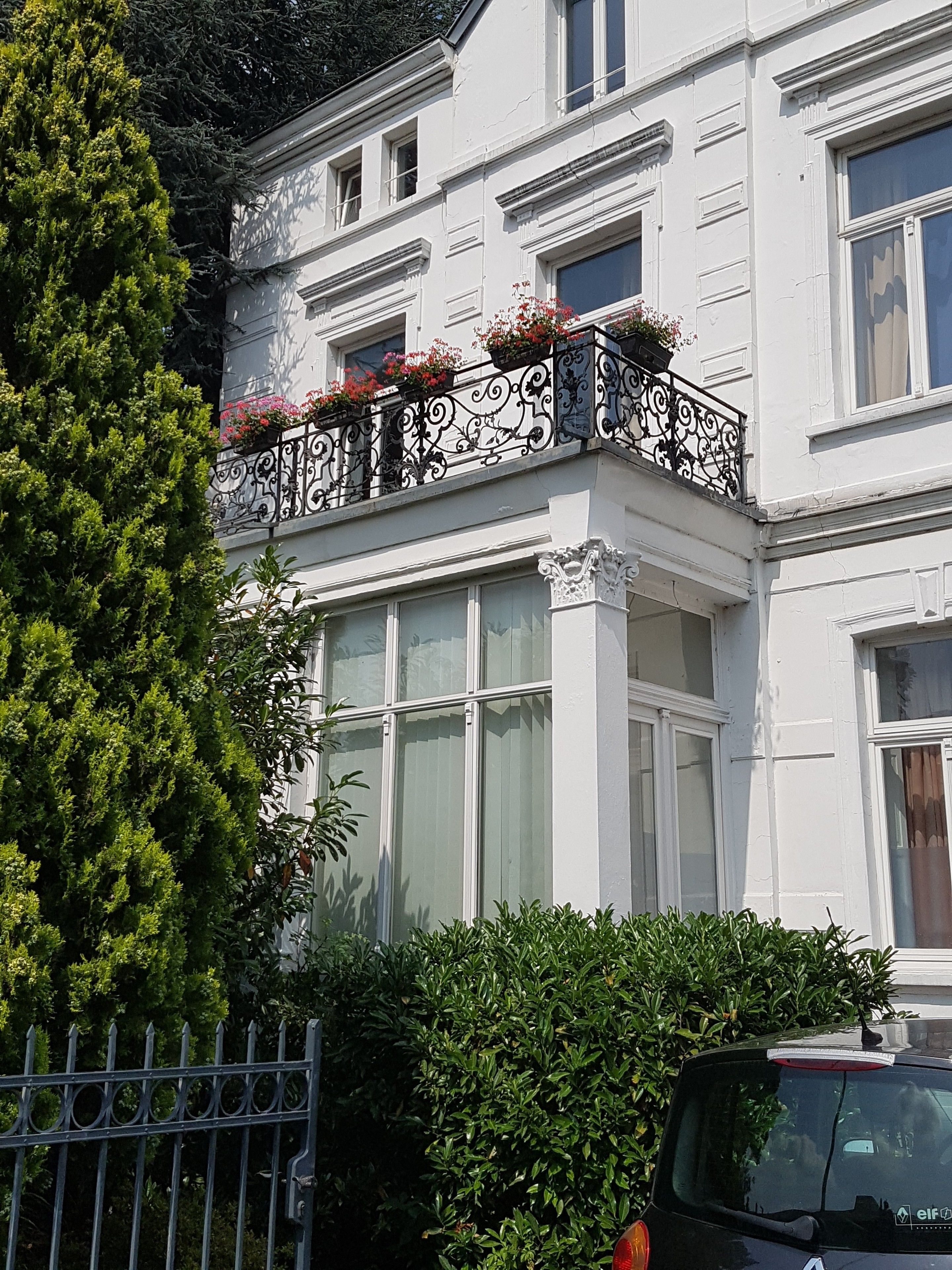 Ein weißes Gebäude mit einem Balkon, der schmiedeeiserne Geländer und Blumenkästen hat.