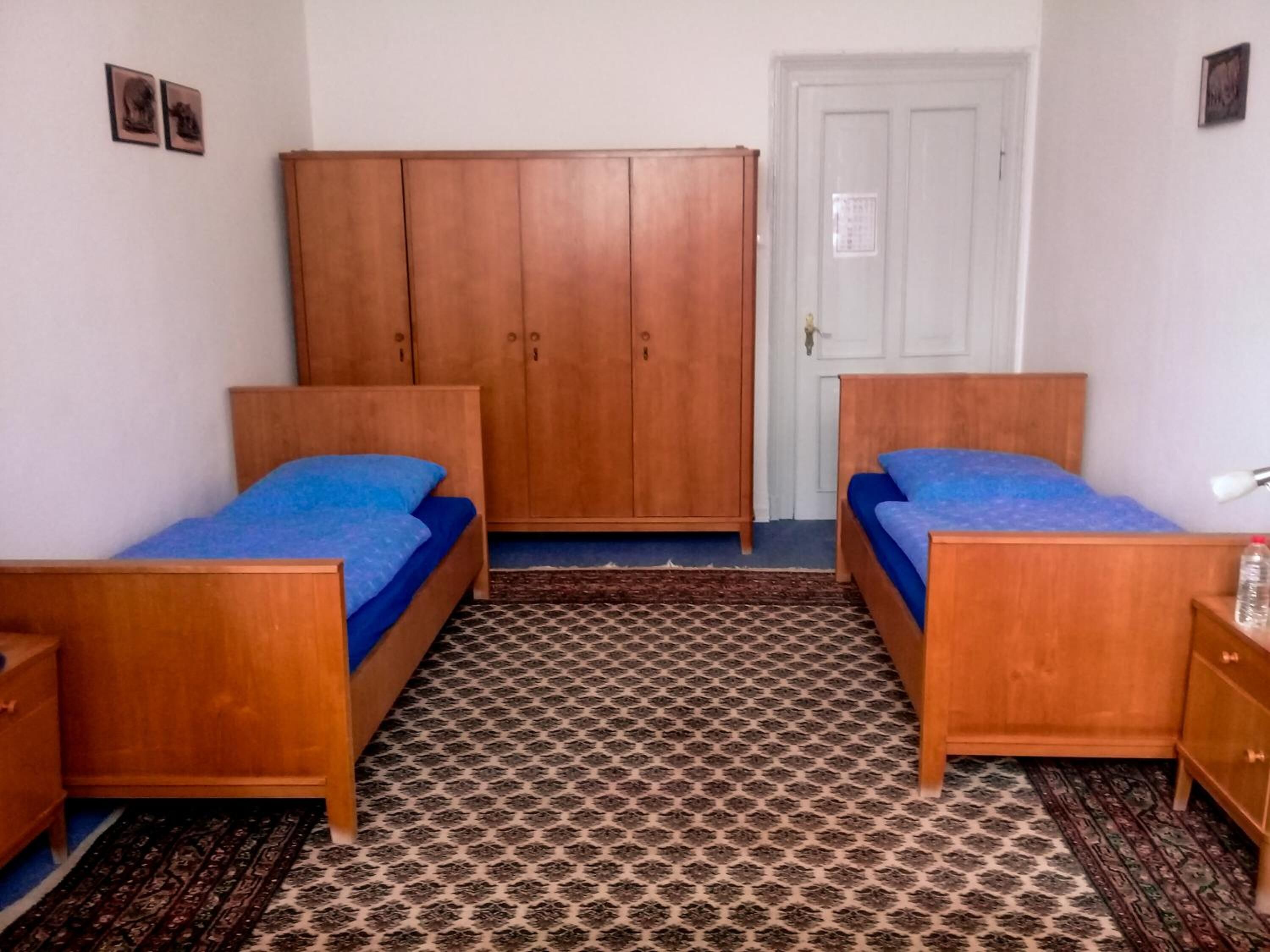 A room with two wooden beds, a wardrobe, and patterned carpet.