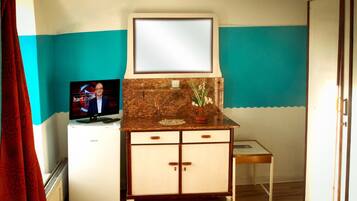 A room with a television on a white cabinet, a small table, and a mirror above the cabinet.