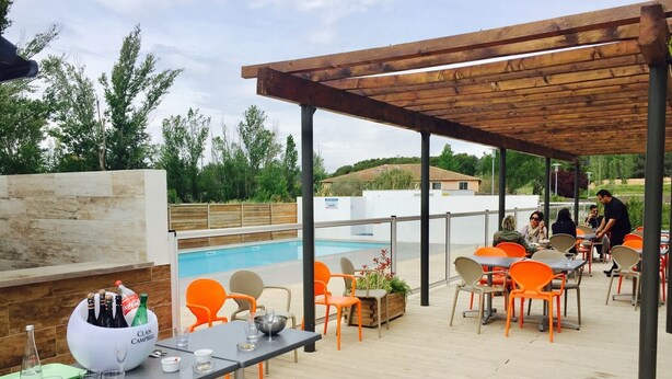 Un área de patio al aire libre con piscina, pérgola de madera y sillas naranjas.