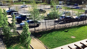 Un estacionamiento con varios coches, un área cercada con árboles y un paseo de baldosas con una planta en maceta.