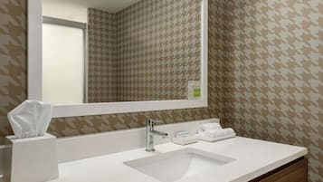 Un baño moderno con un espejo grande, lavamanos blanco y papel tapiz estampado.