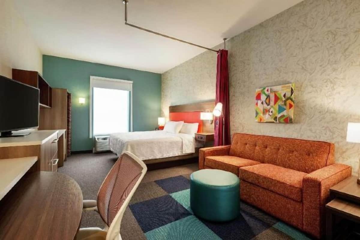 Ein Hotelzimmer mit Bett, einer Couch, einem Schreibtisch, einem Fernseher und einem Bild an der Wand.