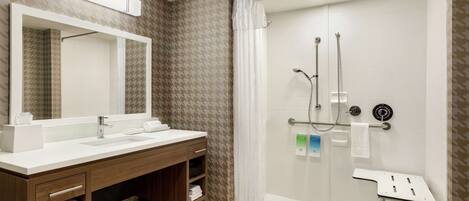 A modern bathroom with a wooden vanity, a large mirror, a glass-enclosed shower, and a towel rack.