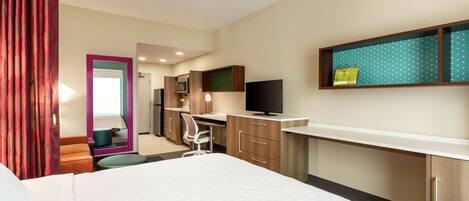A hotel room with a bed, a desk, a chair, a TV, and a kitchenette.