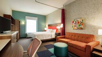 A hotel room with a bed, a sofa, a TV, a desk, and a chair.