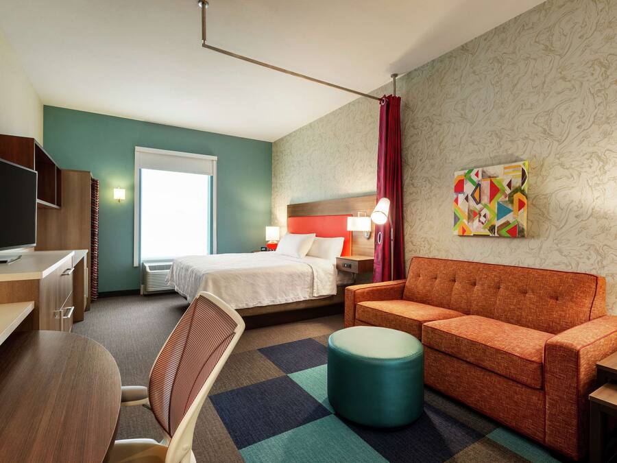 A hotel room with a bed, a sofa, a TV, a desk, and a chair.