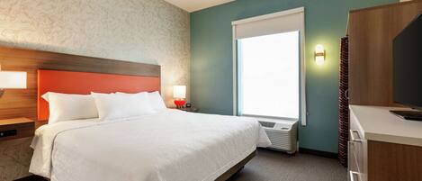 A hotel room with a large bed, a wooden headboard, a nightstand with a lamp, a window with blinds, and a television on a stand.