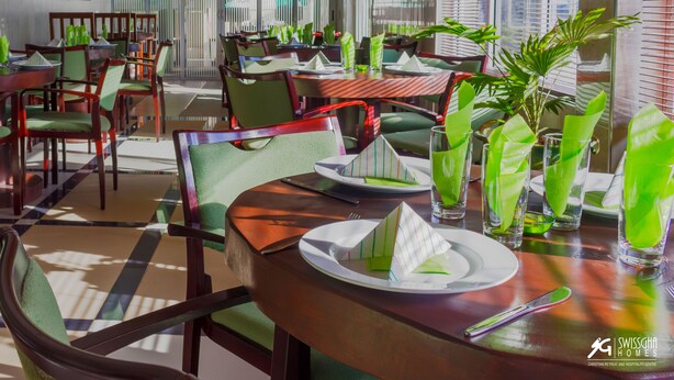 A dining area with tables set for two, featuring green chairs and neatly arranged table settings. - SwissGha Homes Christian Retreat and Hospitality Center (Tema)
