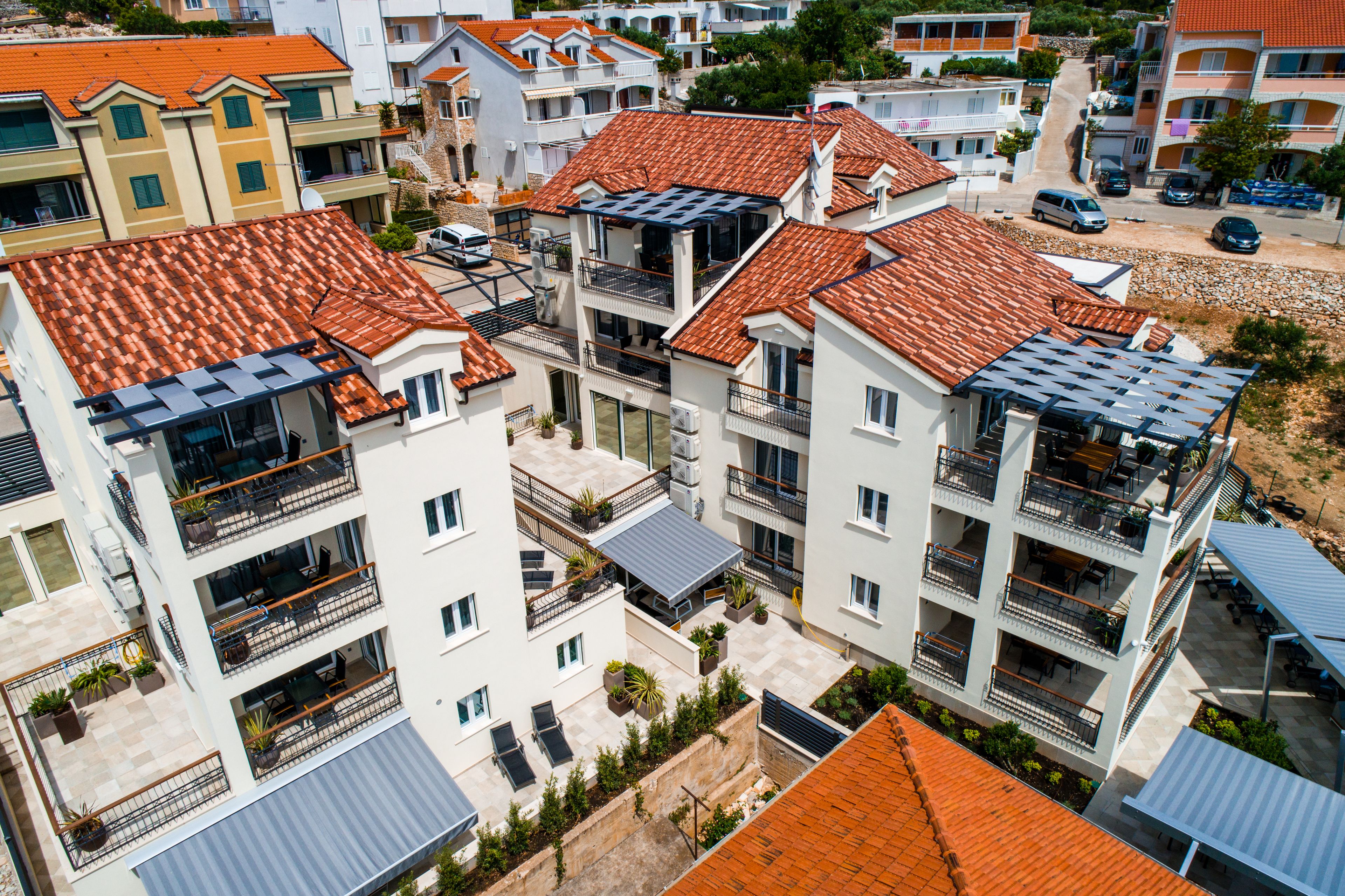 A multi-story residential building with balconies, a covered outdoor seating area, and a paved courtyard.