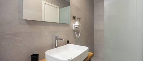 A modern bathroom with a large rectangular sink, a mirror, and a shower.