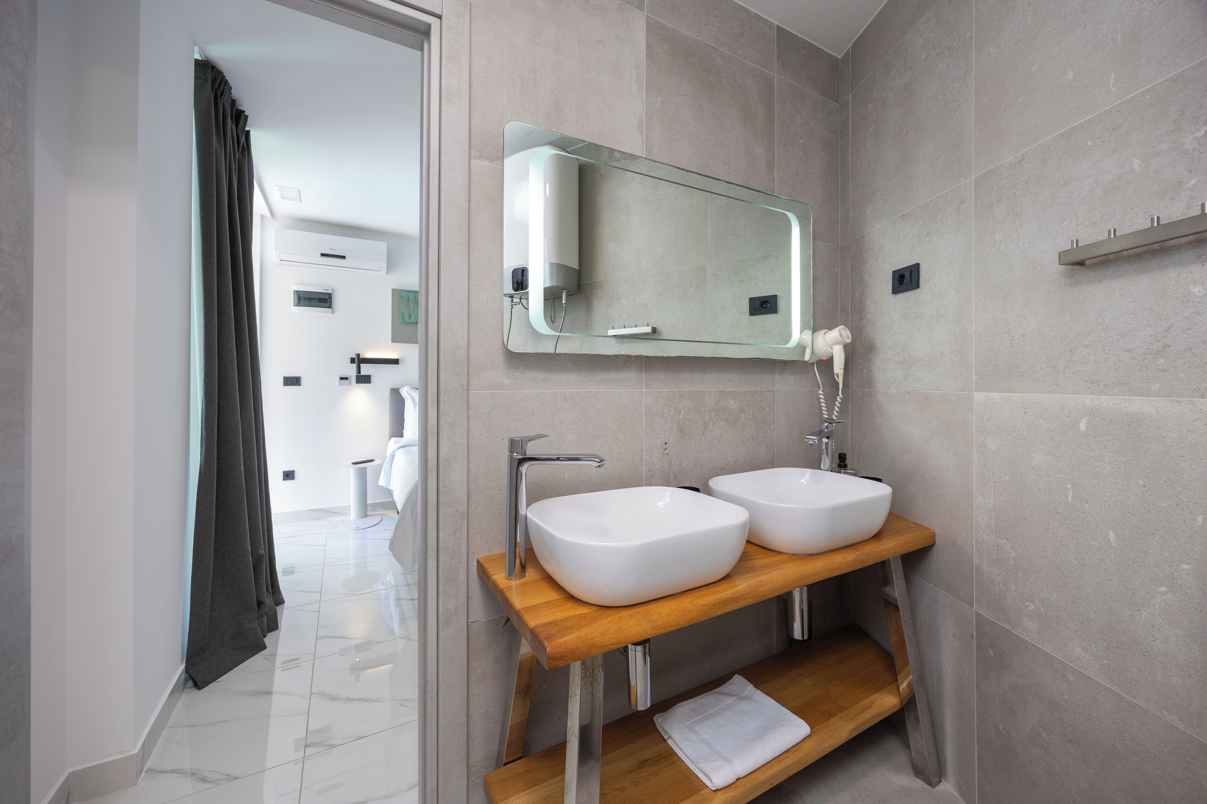 A modern bathroom with two white sinks, a wooden vanity, a glass mirror, and a towel on the shelf.