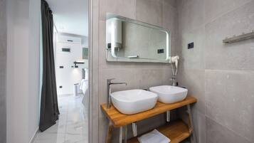 A modern bathroom with two white sinks, a wooden vanity, a glass mirror, and a towel on the shelf.