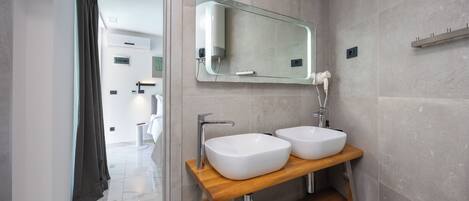 A modern bathroom with two white sinks, a wooden vanity, a glass mirror, and a towel on the shelf.