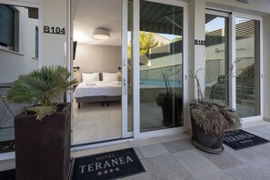 A hotel entrance with a bed visible inside, a pool, and potted plants outside. - Hotel Teranea (Hvar)