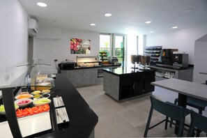 A modern kitchen with a buffet setup, a coffee machine, and a dining area with chairs. - Hotel Teranea (Hvar)