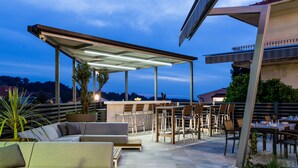 An outdoor patio area with seating, a bar, and a view of the surrounding landscape. - Hotel Teranea (Hvar)