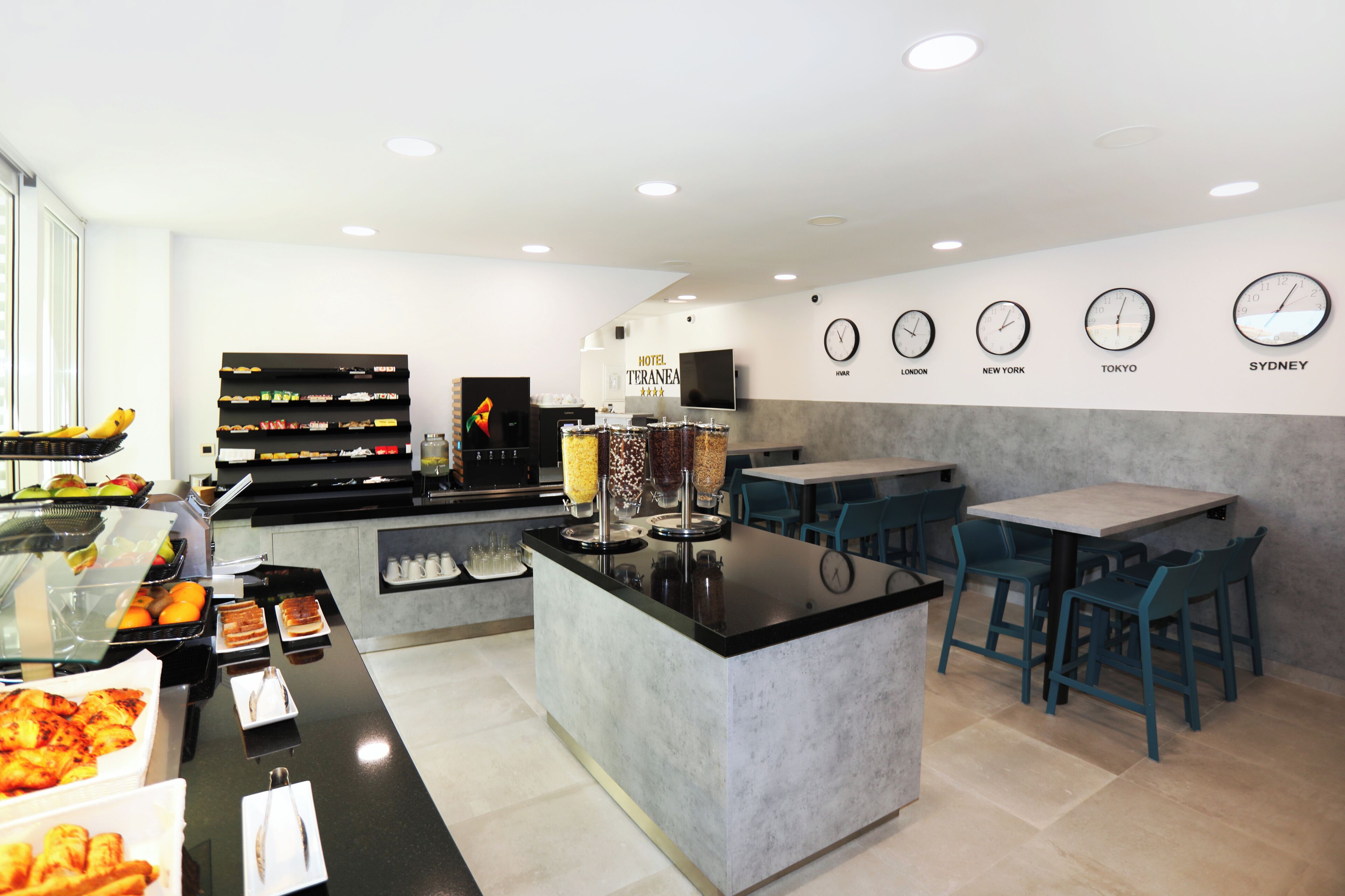 A hotel breakfast area with a buffet, seating, and clocks indicating different cities.
