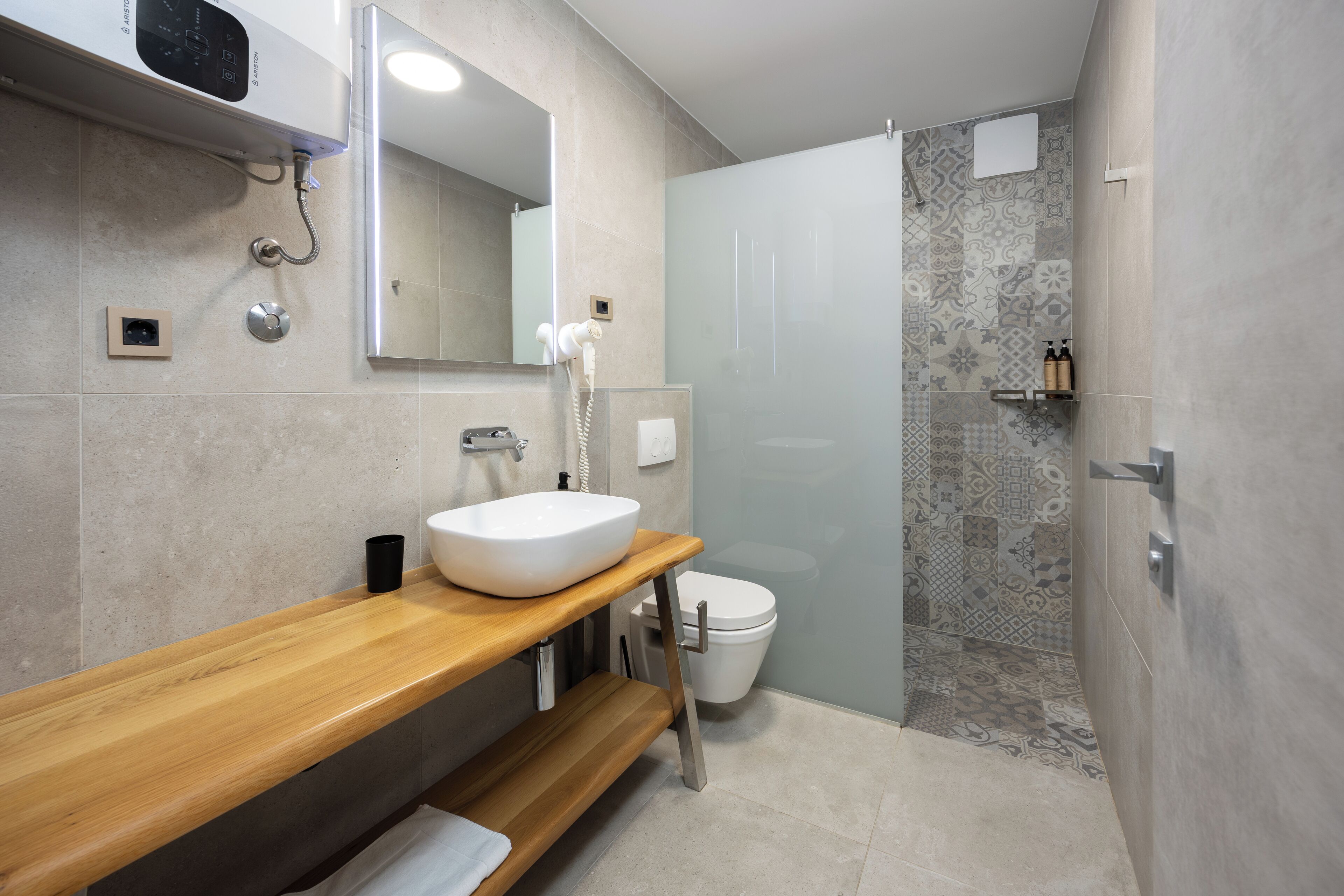 Une salle de bain moderne avec un meuble-lavabo en bois, un lavabo blanc, des toilettes et un espace douche agrémenté de carreaux à motifs.
