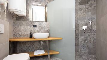 A modern bathroom with a white toilet, a wooden vanity with a white sink, a glass shower enclosure, and patterned tiles.
