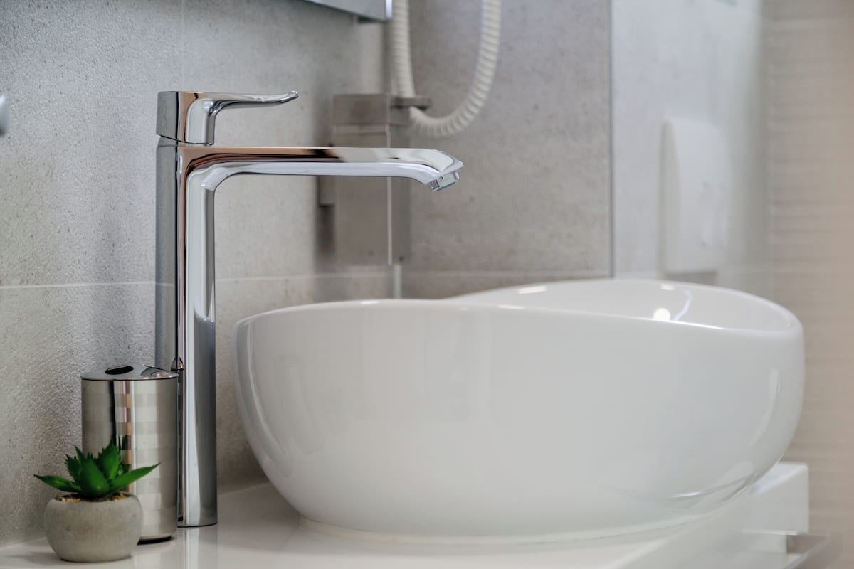 Un baño moderno con un lavamanos grande de color blanco, grifo cromado y una pequeña planta en maceta.