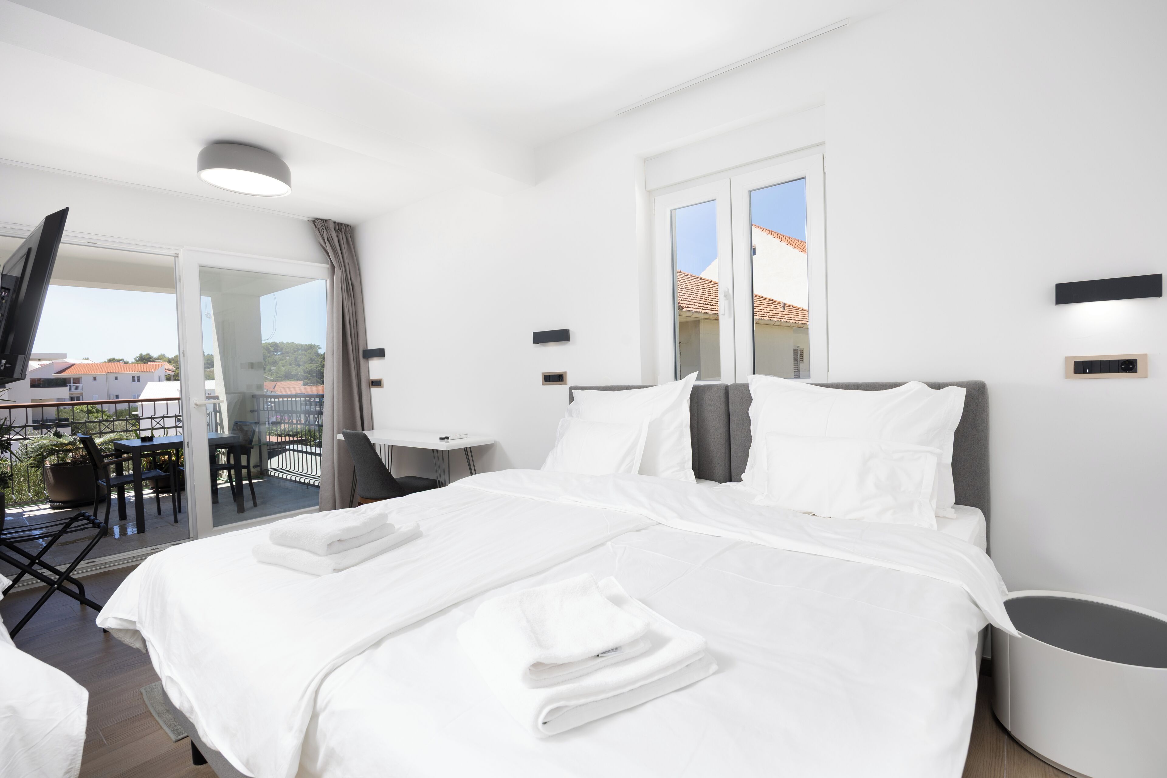 Een moderne hotelkamer met een groot bed, een bureau en een balkon met zitplaatsen.