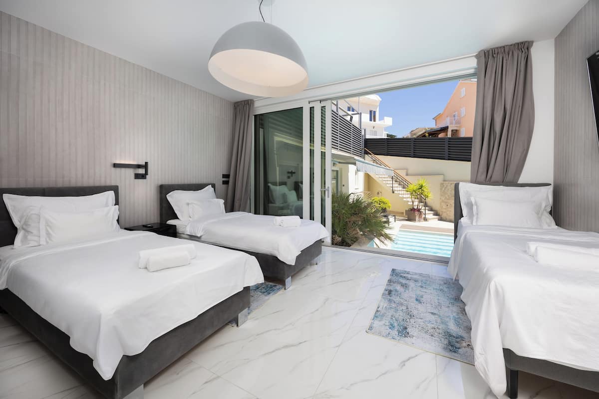 Habitación de hotel moderna con dos camas, un ventanal grande y vista a una piscina.