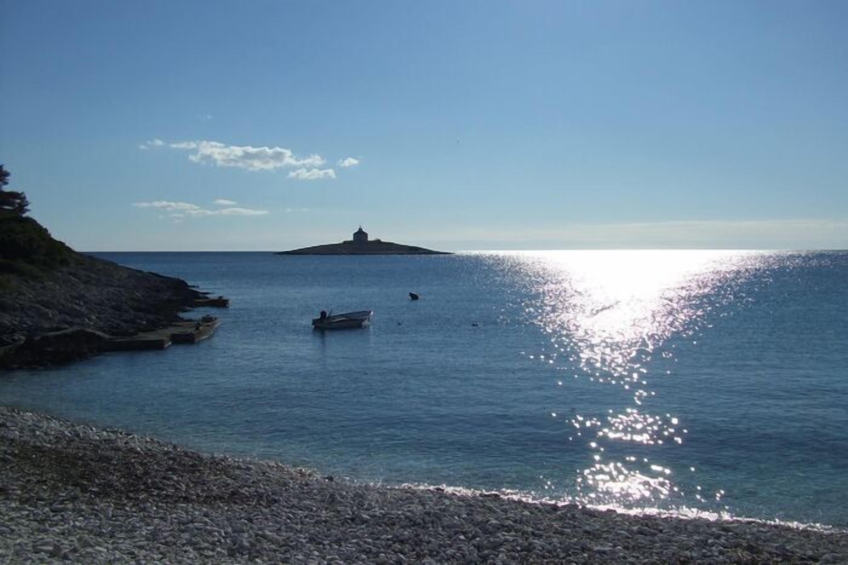 Escena costera con costa rocosa, mar tranquilo y una isla distante con una construcción.