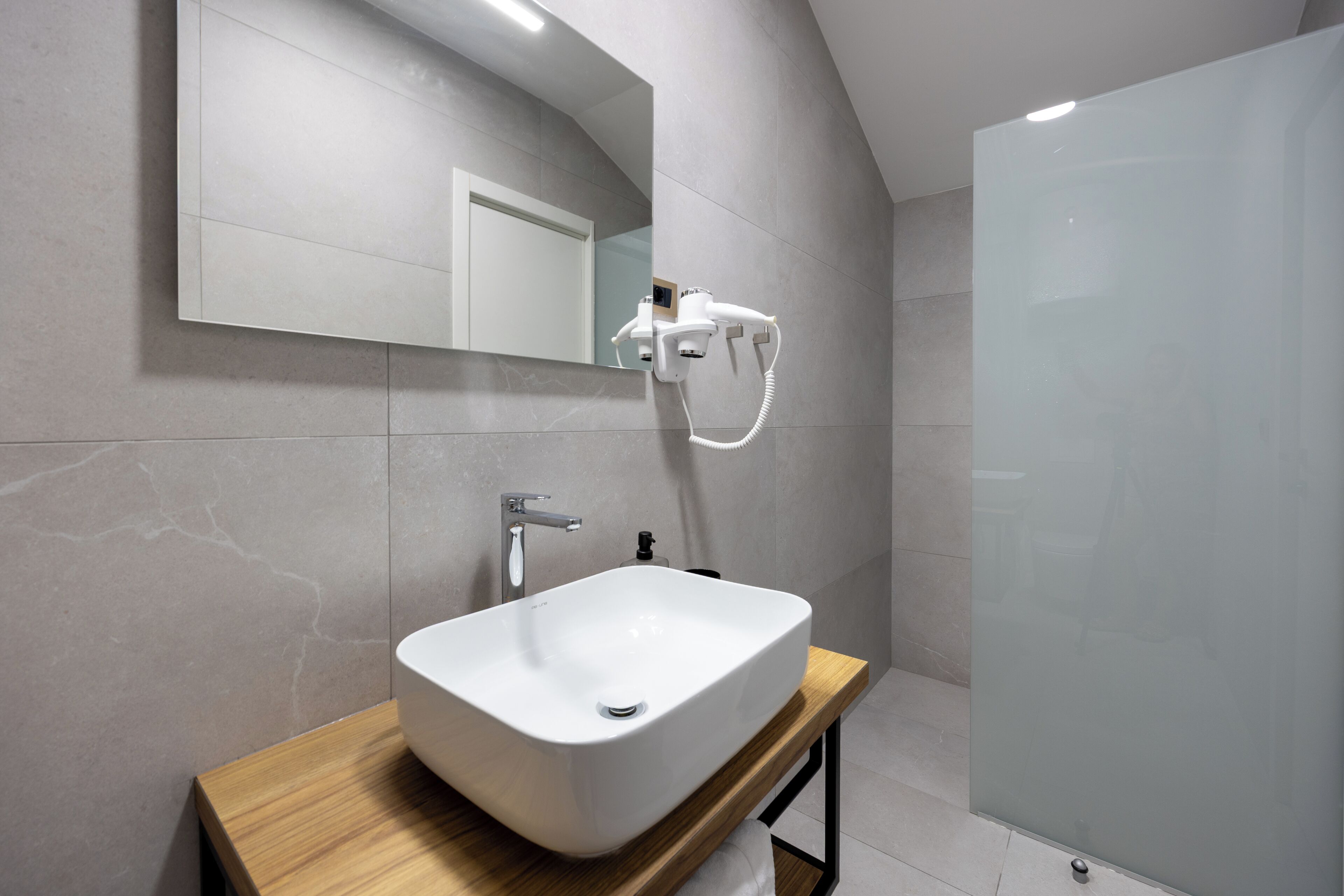 A modern bathroom with a large mirror, a white sink, and a handheld showerhead.