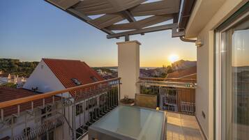 Un balcón con una mesa y sillas de vidrio, con vista a un paisaje urbano con edificios y un atardecer.