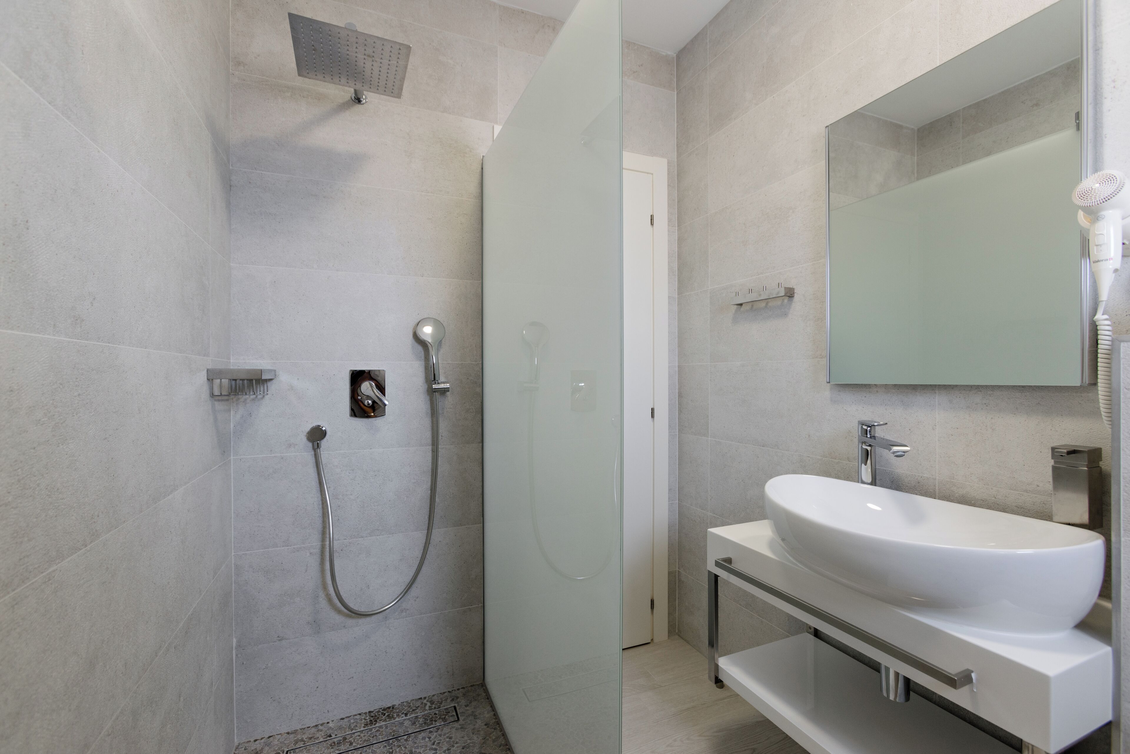 Un baño moderno con cabina de ducha de vidrio, un lavabo blanco y un espejo grande.