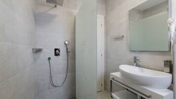 Un baño moderno con cabina de ducha de vidrio, un lavabo blanco y un espejo grande.